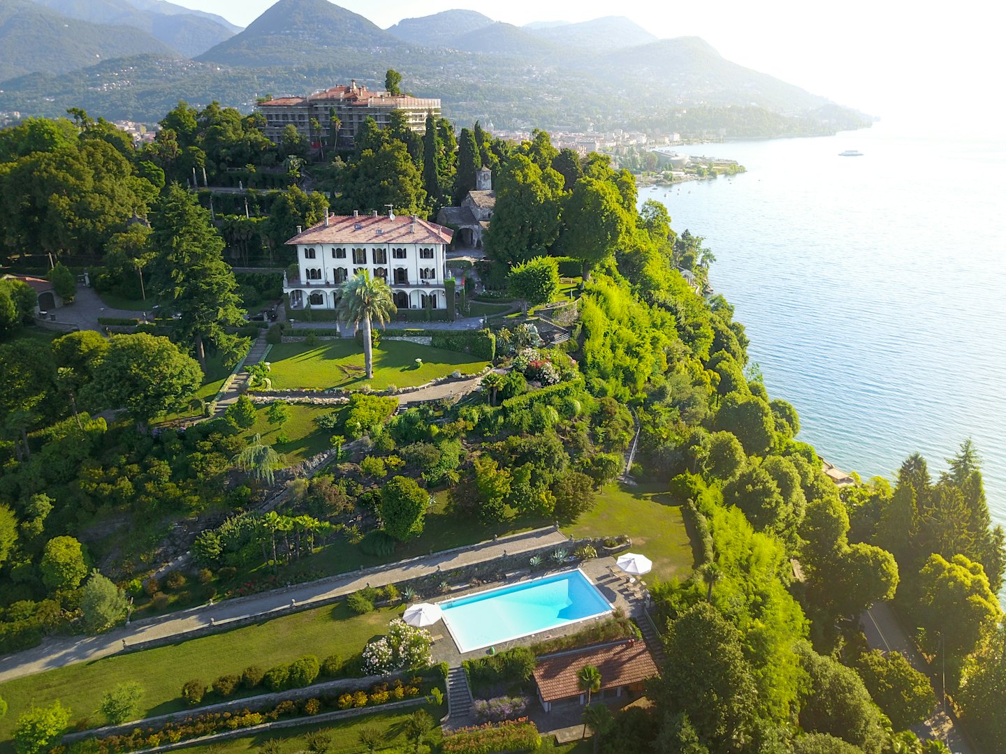 White villa on green hillside overlooking infinity pool and lake.