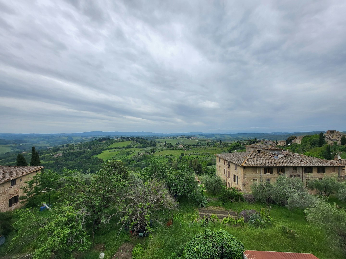 Rolling green hills feature vineyards and stone buildings under overcast skies.