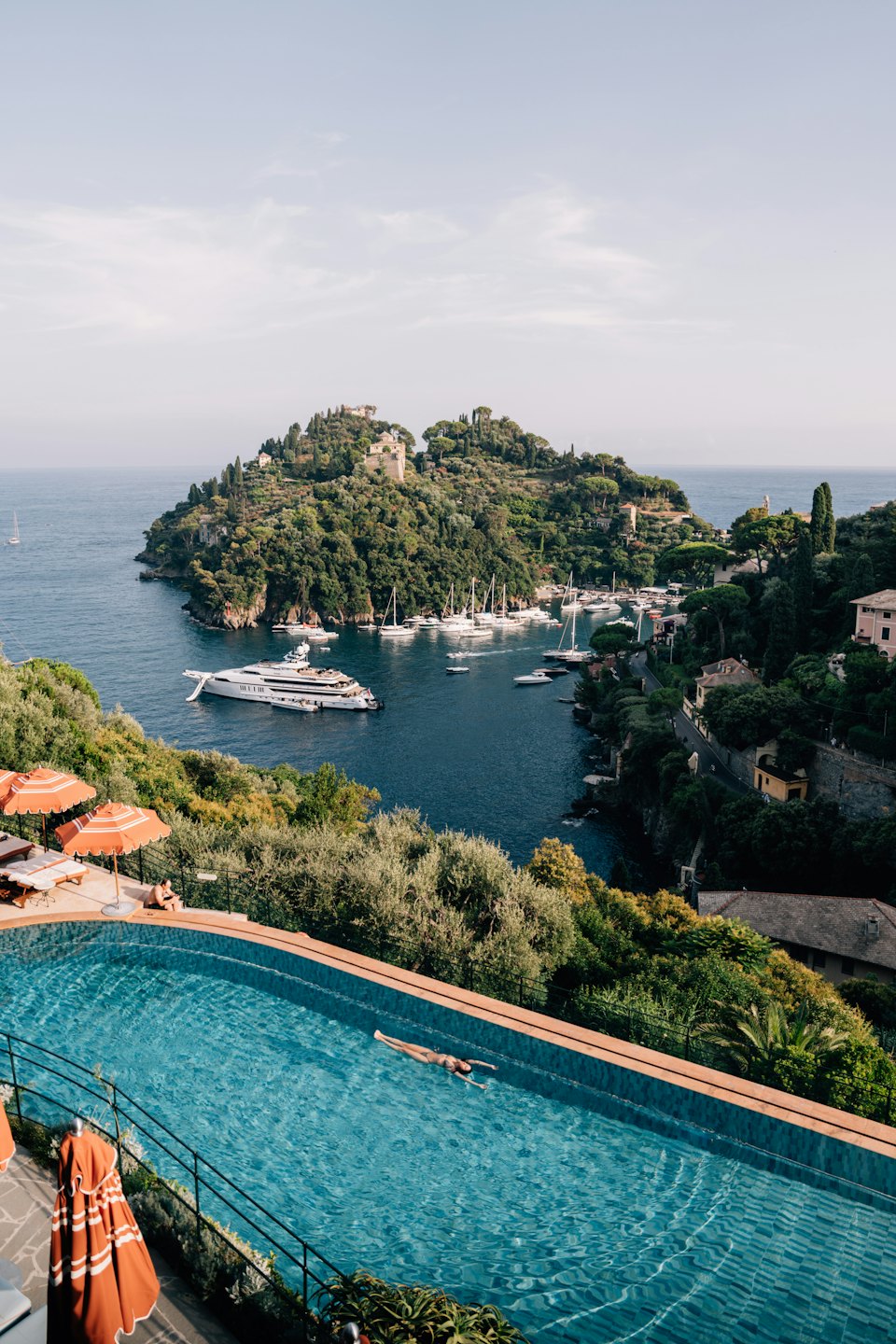 A person floats in an infinity pool overlooking a Mediterranean bay.