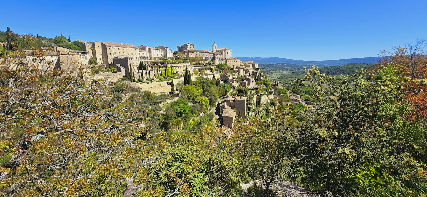 Sunlit stone village with terracotta roofs on a green hilltop.