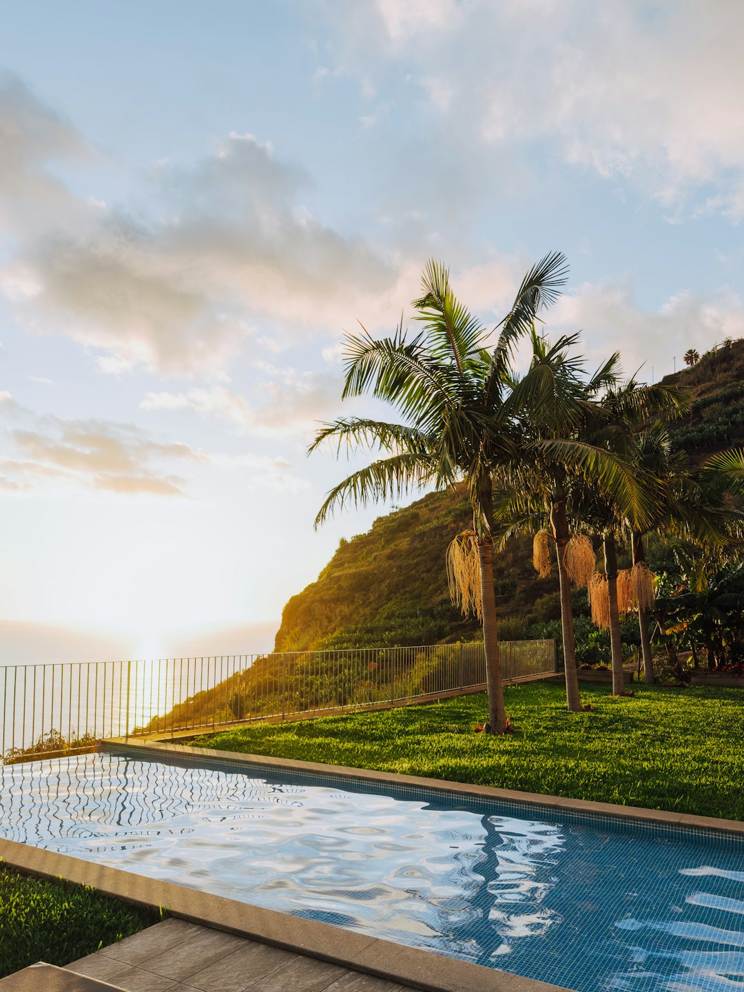Infinity pool with blue tiles overlooks the ocean at sunset.