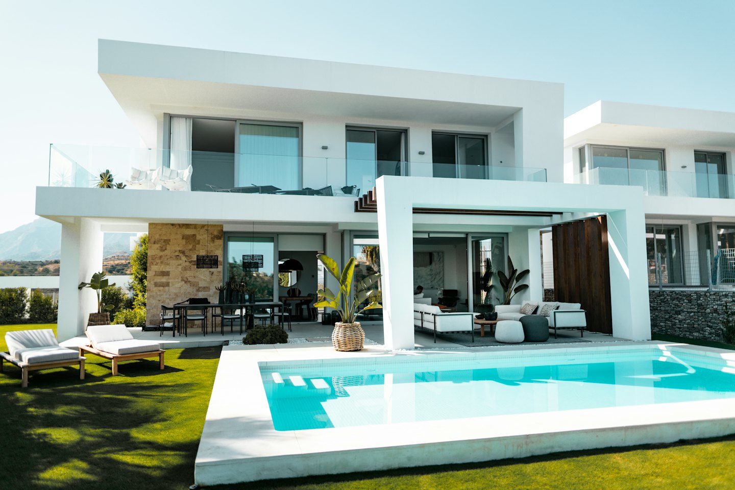 Modern white villa with pool and lawn on a sunny day.
