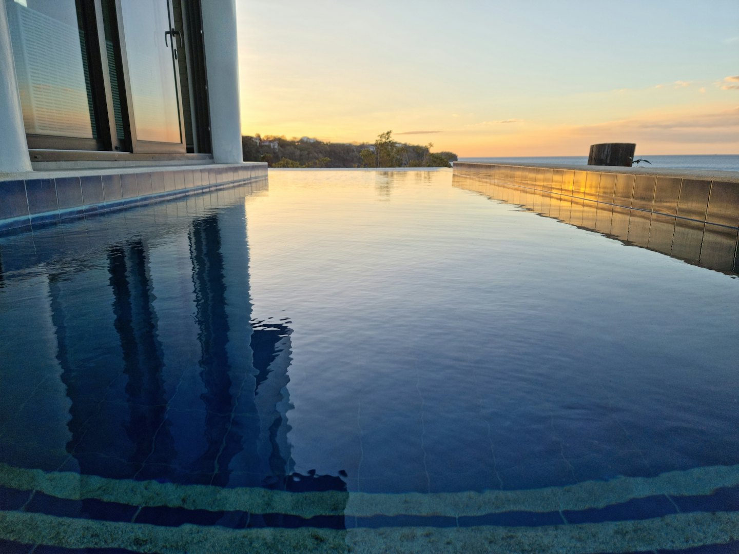 Infinity pool reflects the sky with hills and ocean beyond.